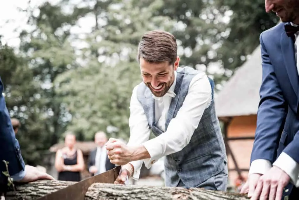 Lachender Bräutigam beim gemeinsamen Baumstammsägen