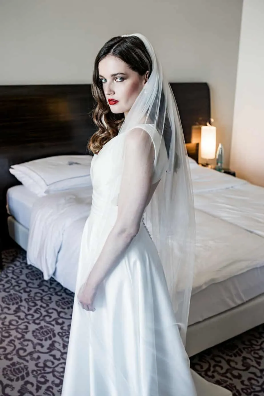 Braut zeigt die Rückansicht ihres Hochzeitskleides im Hotelzimmer