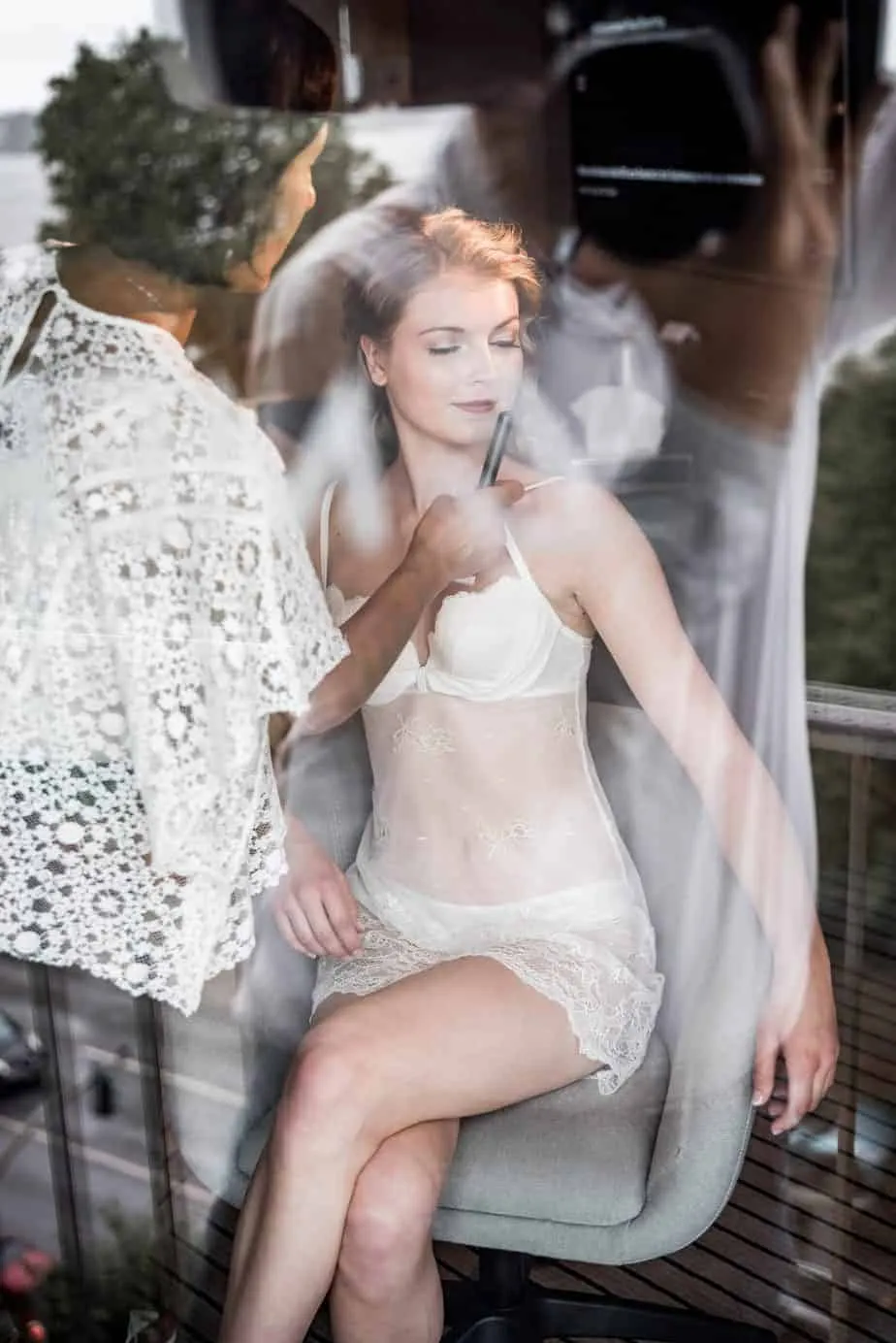 Braut wird durch eine Fensterscheibe beim Make-up fotografiert