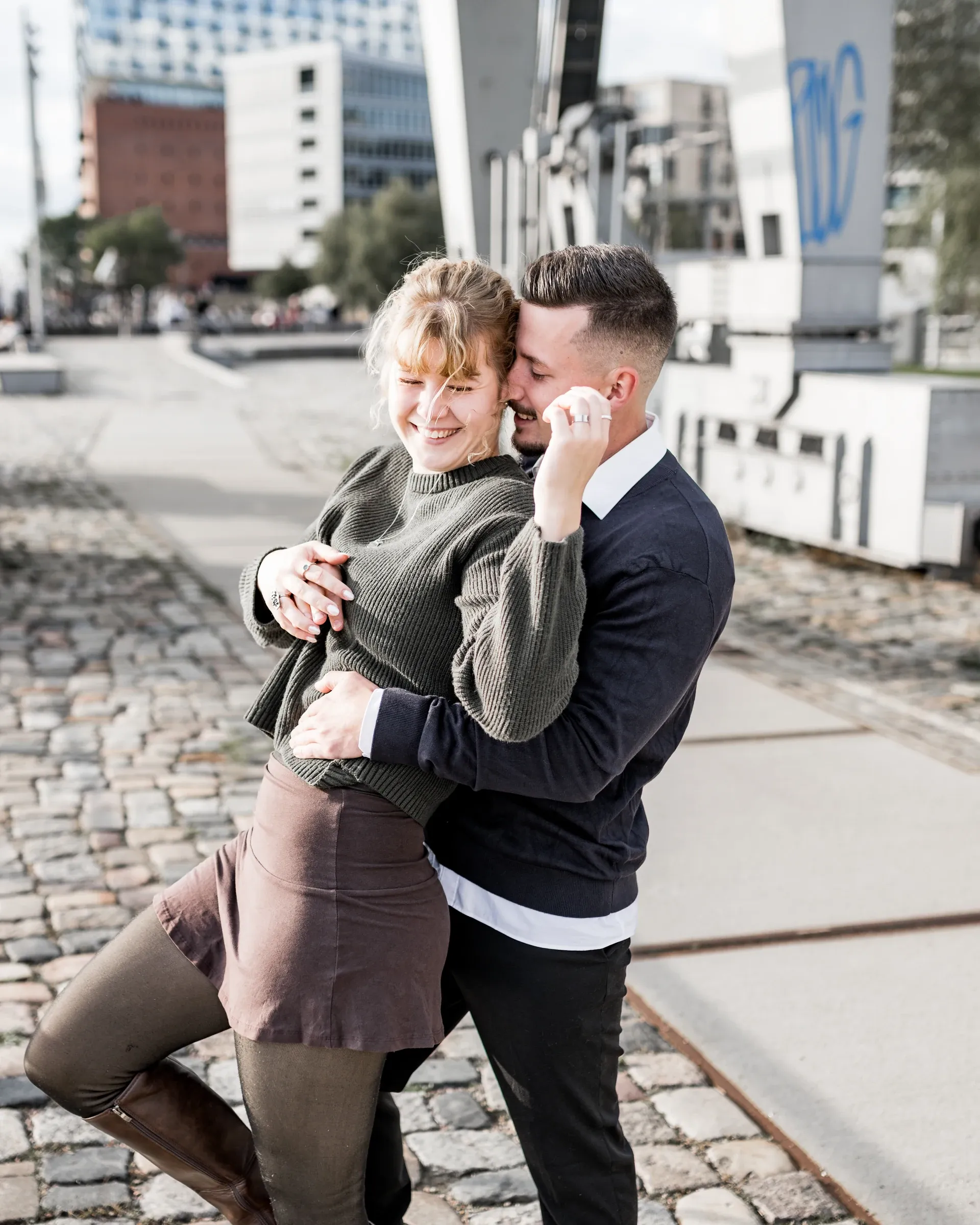 Liza und Domenic lachen auf dem Kopfsteinpflaster am Wasser