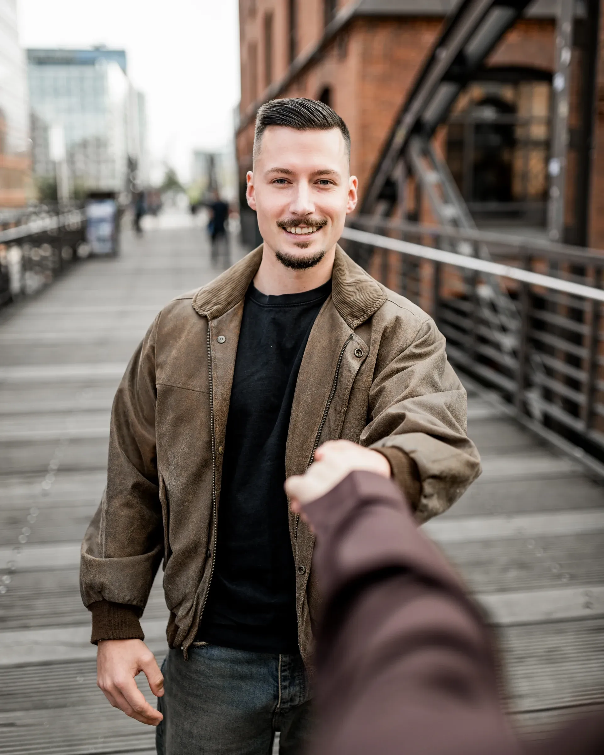 Domenic reicht lächelnd eine Hand auf der Brücke in der Speicherstadt