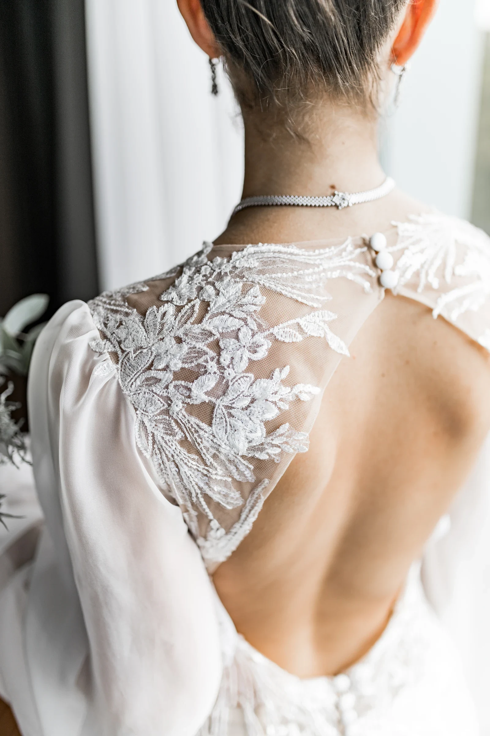 Detailaufnahme von der Rückenansicht einer Braut in einem Hochzeitskleid mit fein gearbeiteten Spitzenapplikationen und Knöpfen an der Schulterpartie