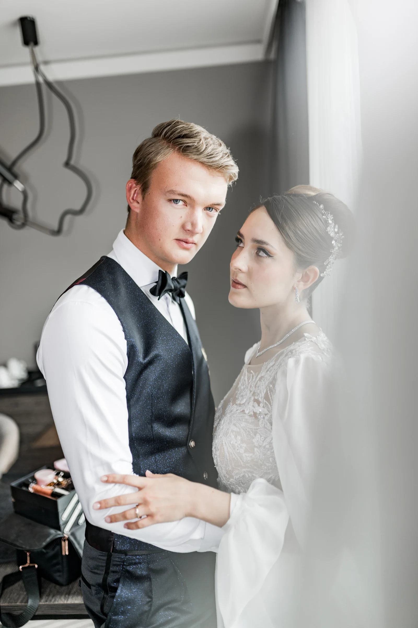 Braut und Bräutigam beim Hochzeitsshooting eng umarmt, er im schwarzen Anzug mit Fliege, sie im weißen Spitzenbrautkleid mit Haarschmuck