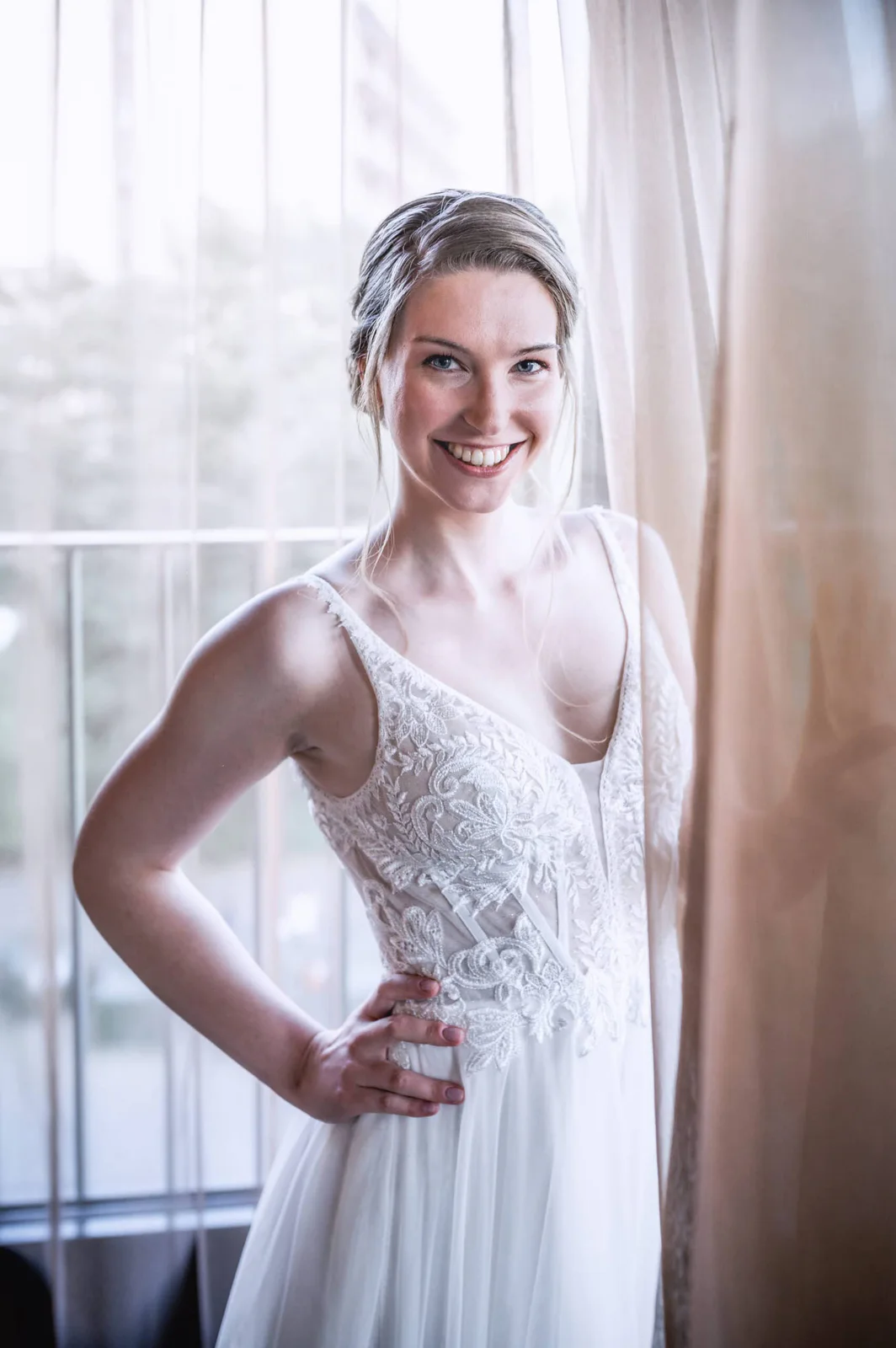 Lachende Braut im Brautkleid vor einem hellen Fenster