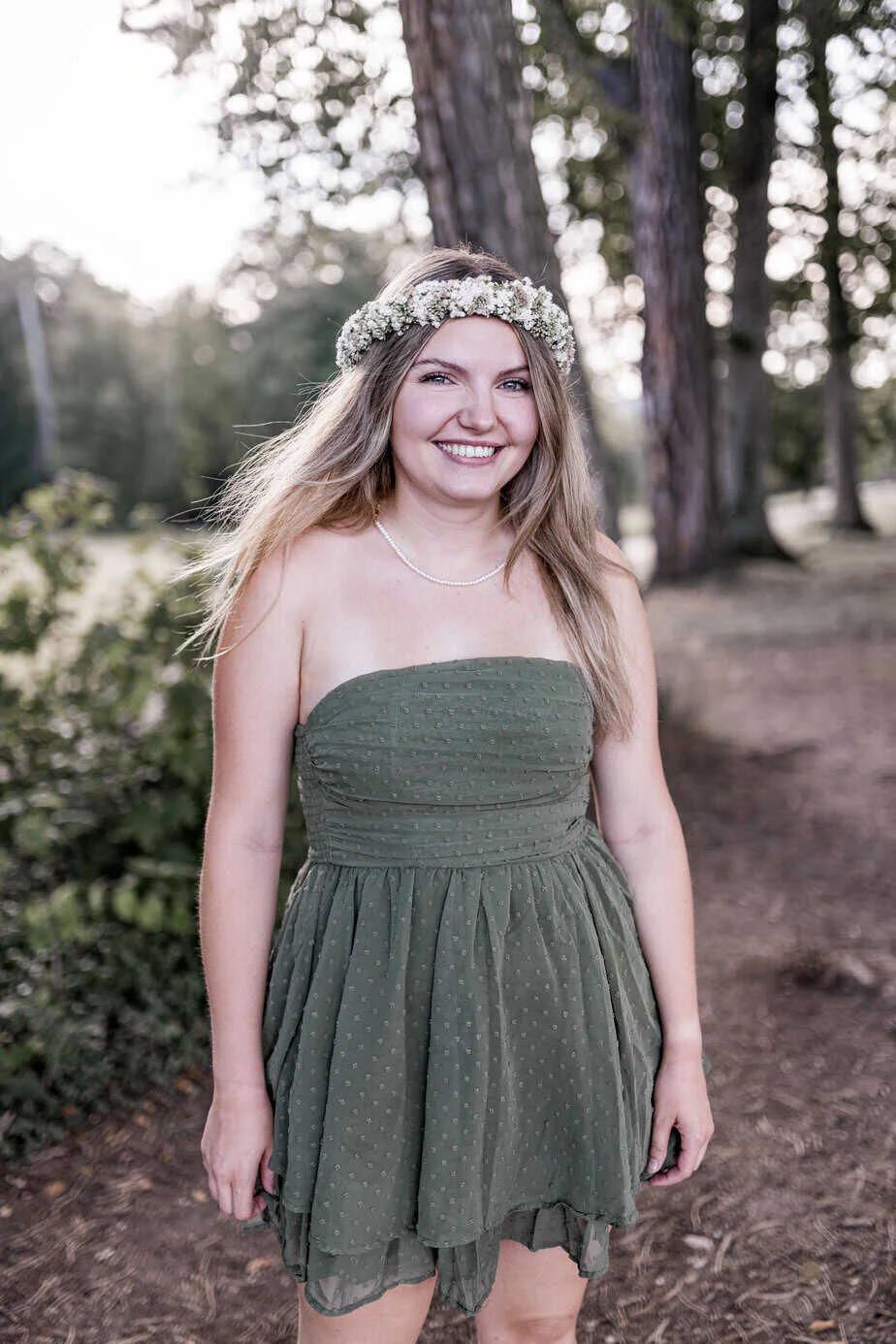 Junge Frau mit Blumenkranz und grünem Kleid im Wald