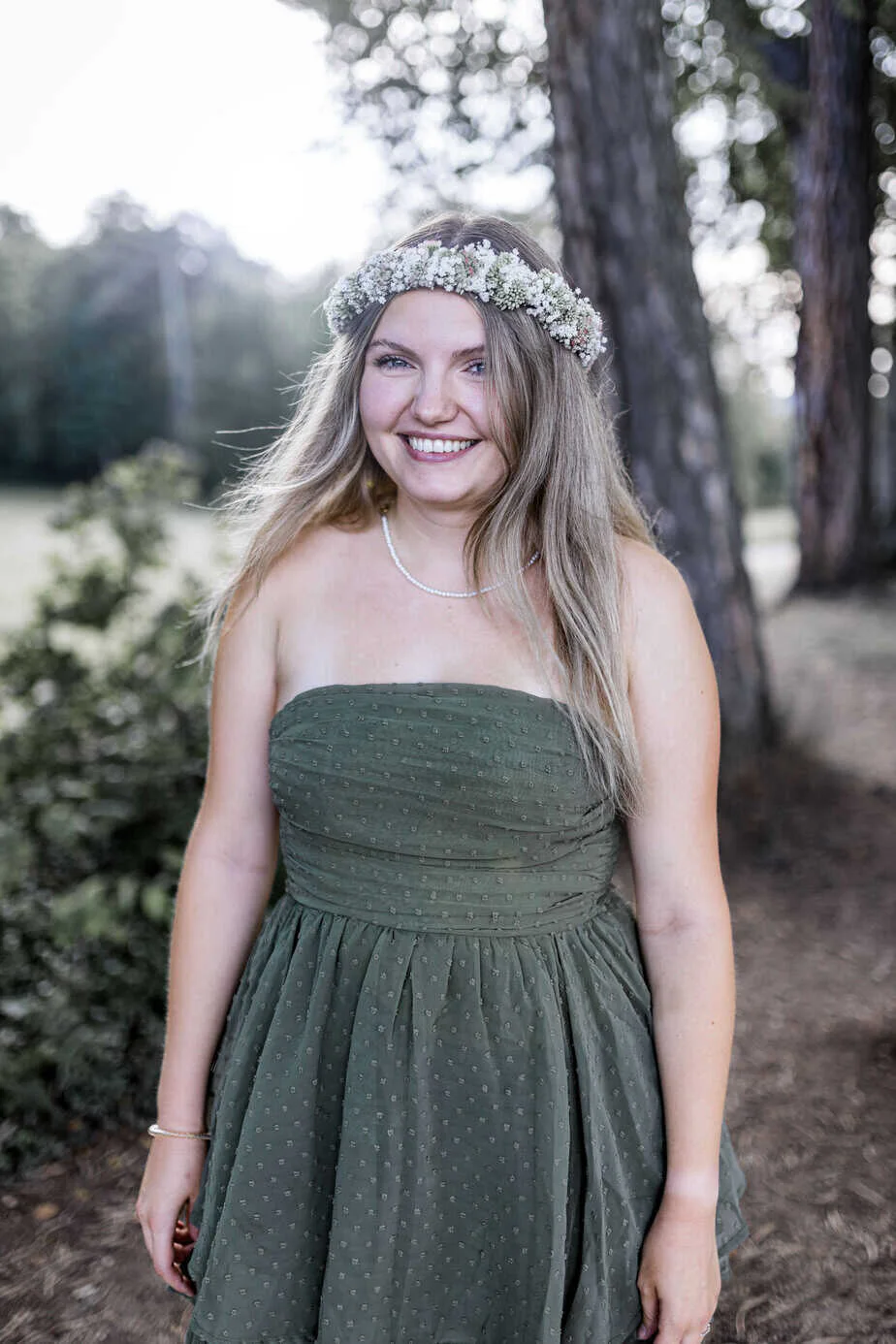 Frau mit Blumenkranz und grünem Kleid zwischen Bäumen