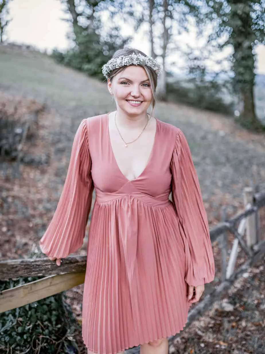 Portrait einer jungen Frau im rosafarbenen Kleid an einem Holzgeländer