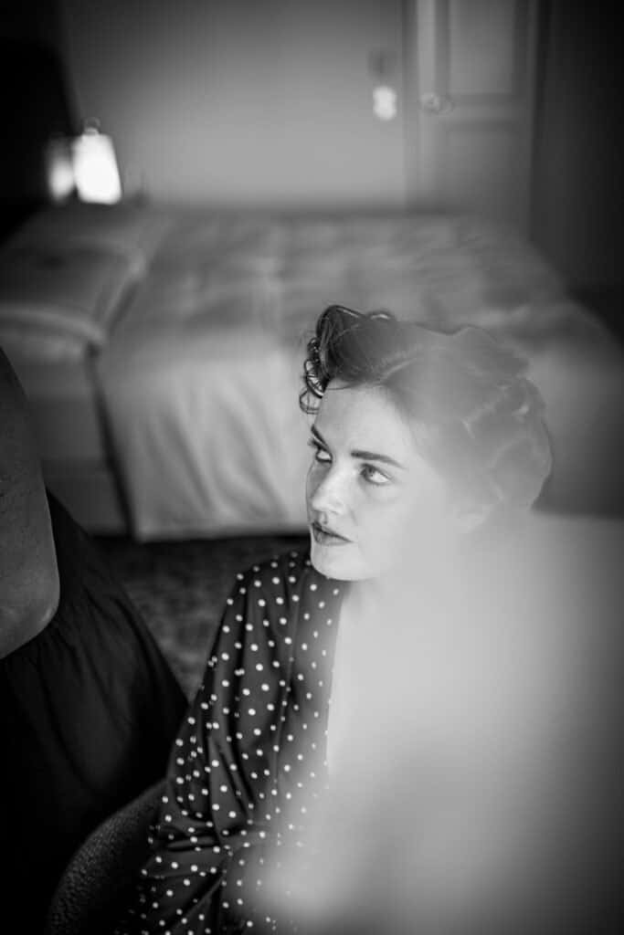 Braut in gepunktetem Morgenmantel, mit einem sanft verschwommenen Hintergrund einer Hotelsuite.