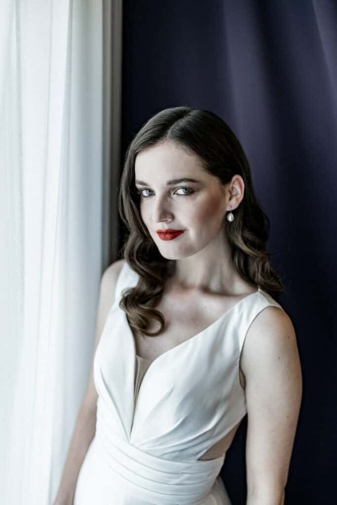 Elegante Frau in Hochzeitskleid vor Fenster mit natürlichem Licht, professionelles Portrait, Piercing, elegante Frisur, kreative Hochzeitsfotografie, Damenmode, Hochzeitsfotograf Berlin.