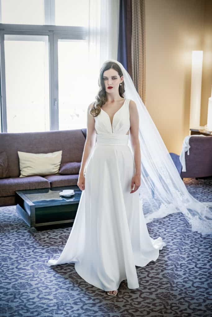 Elegantes Brautkleid mit V-Ausschnitt, moderne Hochzeitsmode, stilvolle Brautfotografie, Hochzeitsbilder in Hotelzimmer, professionelle Hochzeitsfotografie Artbild-Fotografie.
