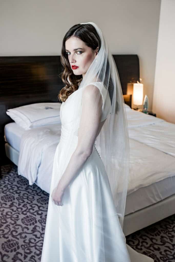 Elegant Braut in weißem Hochzeitskleid mit Schleier, modernes Hochzeitsfotografie, professionelles Bridal Shooting, stilvolle Hochzeitsfotos, kreative Hochzeitsfotografie in Hotelzimmer.