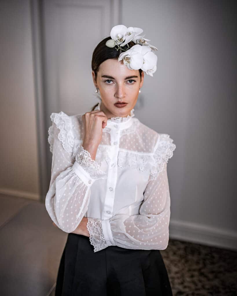 Elegantes Portrait einer Frau mit weißen Orchideen als Haarschmuck, stilvolle Kleidung und ausdrucksstarkem Blick, professionelle Modefotografie, künstlerische Lichtführung, perfekter Ausdruck.