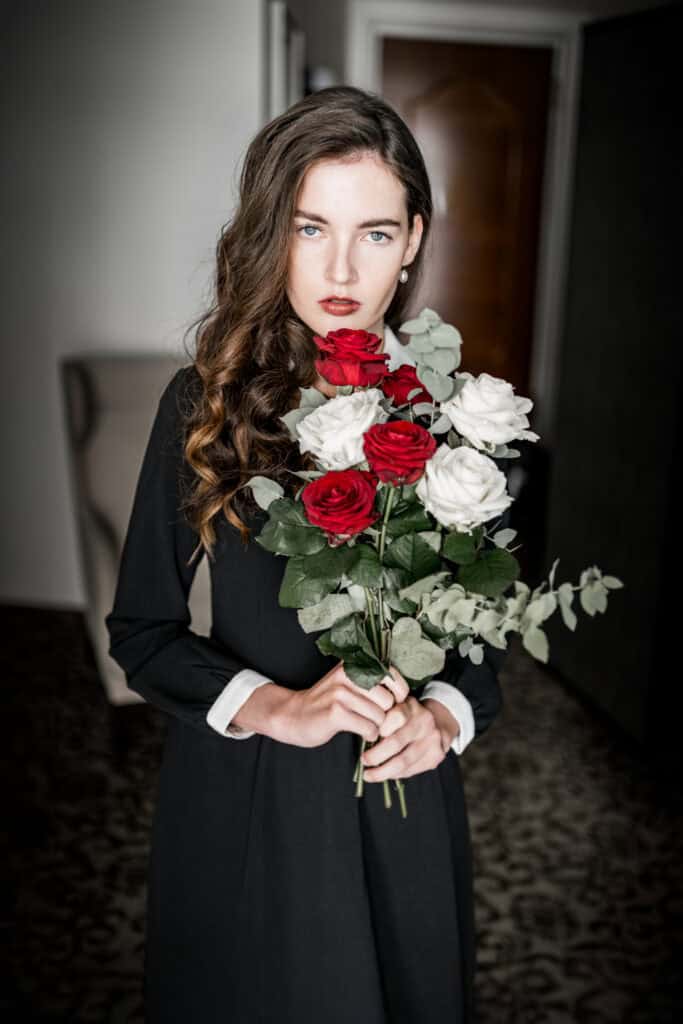 Blumenstrauß mit weißen und roten Rosen, gehalten von einer elegant gekleideten Frau, Nahaufnahme, Hochzeits- oder Porträtfotografie, stilvoller Bildausschnitt, künstlerisches Fotodesign.