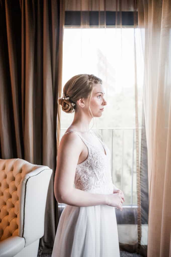 Braut im weißen Brautkleid schaut aus dem Fenster